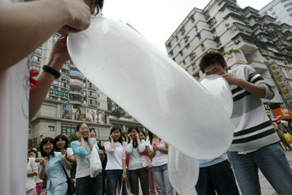 A participant blows up a condom as others look on during a condom-blowing contest held in southwest China's Chongqing Municipality May 28, 2006. The contest, which aims at establishing people's knowledge of safe sex, attracted many local residents. A university student won the contest by bursting a condom within one minute, China Daily reported. Picture taken May 28, 2006.