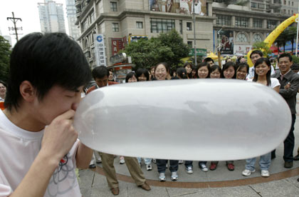 A participant blows up a condom as others look on during a condom-blowing contest held in southwest China's Chongqing Municipality May 28, 2006. The contest, which aims at establishing people's knowledge of safe sex, attracted many local residents. A university student won the contest by bursting a condom within one minute, China Daily reported. Picture taken May 28, 2006.