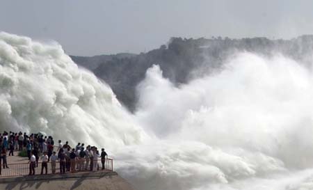 Visitors look at the water gushing from Xiaolangdi Reservoir on the Yellow River in Central China's Henan Province June 15, 2006. About 3000 cubic meters per second of water will be discharged out of the reservoir for next 15 days to wash the sands in the riverbed into the sea. [newsphoto]