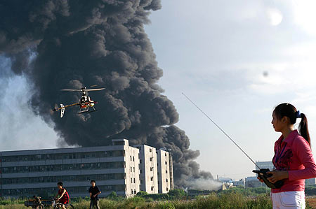 A girl plays a remote-control plane toy as smoke billows out from a shoe plant in Shenzhen south China's Guangdong Province, after a fire broke out there. The blaze lasted 12 hours before it was finally put out, engulfing a warehouse and a workshop. No casualty was reported. [gd.southcn.com]