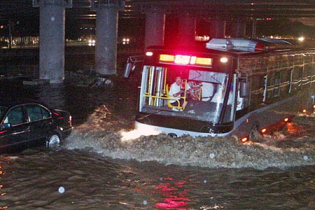 A car moves forward on a flooded street in Beijing, July 24, 2006. Beijing Meteorological Bureau raised rainstorm alarms twice on Tuesday. [Luo Xiaoguang/Xinhua] 