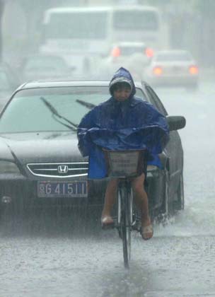 A Chinese cyclist passes a car in rain on a street in Beijing,July 24, 2006. Beijing Meteorological Bureau raised rainstorm alarms twice on Tuesday. [Luo Xiaoguang/Xinhua]