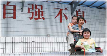 Mother Guo Qingmei stands behind Wang Yan on the wheel chair while carrying Wang Rui on the back. The Chinese characters on the wall read Zi Qiang Bu Xi, which means "never stop trying." 