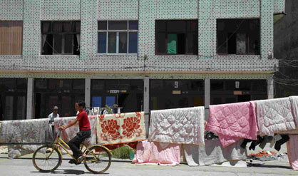 A man rides his bicycle in front of blankets hung up to dry following Typhoon Saomai in Jinxiang, China's eastern province of Zhejiang August 13, 2006. Three days after the huge storm barrelled into the coastal provinces of Zhejiang and Fujian, the official death toll has risen to 114 with at least 183 missing. 