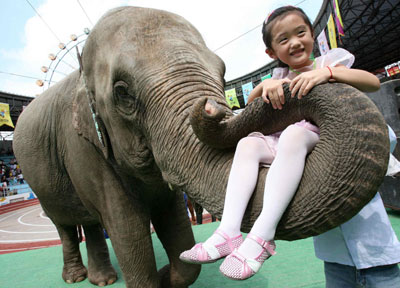 A girl poses for a picture on an elephant's trunk during an animals "Olympics" performance in the Shanghai Wild Animal Park September 28, 2006.