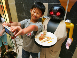 A boy takes a photo with Robot No.2 at a restaurant called Robot Kitchen in Hong Kong October 14, 2006. Robot No.2, which is designed as a female robot and is supposed to deliver dishes, is currently undergoing repairs. The owners say that this is the first such restaurant in the world.