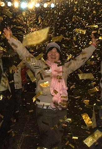 A Chinese woman is surrounded by golden confetti during a event launching colored wrist bands for the 2008 Olympic Games held to coincide with a new year count-down in Beijing, China, Monday, Jan 1, 2007. (AP Photo