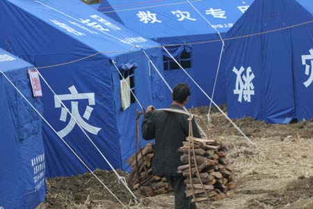 A man carries wood into near the tents on Wednesday following a cave-in at Haijie Village, Nuotong Township, Guangxi Zhuang Autonomous Region, January 3,2007. The cave-in was caused by underground work on a nearby railway tunnel. Nobody was injured in the accident and some 257 villagers were evacuated to safe areas. [newsphoto]