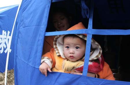 A boy looks out of a tent following a cave-in at Haijie Village, Nuotong Township, Guangxi Zhuang Autonomous Region, January 3,2007. The cave-in was caused by underground work on a nearby railway tunnel. Nobody was injured in the accident and some 257 villagers were evacuated to safe areas. [newsphoto]