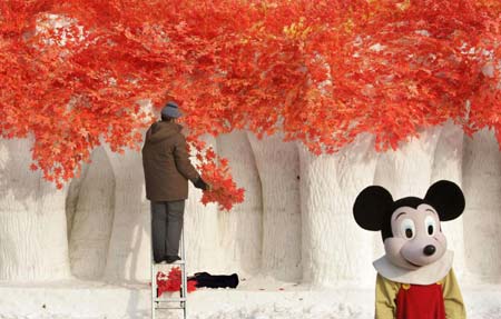 An elderly man prepares a snow sculpture for the upcoming the China Harbin international ice and snow festival as a girl dressed as Mickey Mouse poses at a park in Harbin, northeastern China's Heilongjiang Province, January 4, 2007. 