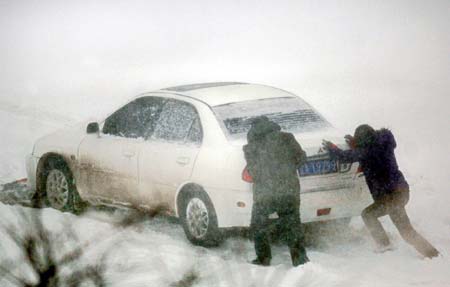 Two residents push a car stranded in snow in Shenyang, Northeast China's Liaoning Province, March 4, 2007. Most vehicles in Shenyang are forbidden to hit the road on Monday except those for public use to ensure the smooth cleanup and transportation of snow, which hit the city on Saturday night and caused major traffic troubles. [Xinhua]