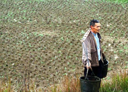 A Chinese farmer carrying water walks near the drying field in Yuping District, Southwest China's Chongqing Municipality March 26, 2007. A total of 13.4 million people and 12 million head of livestock across China are suffering from drinking water shortages due to prolonged drought, statistics released on Wednesday have shown. The State Flood Control and Drought Relief Headquarters (SFCDRH) sources said that, since mid-March, only ten millimeters of rainfall were recorded in Sichuan and Hainan provinces and Chongqing Municipality, and none at all in Yunnan. [Xinhua]