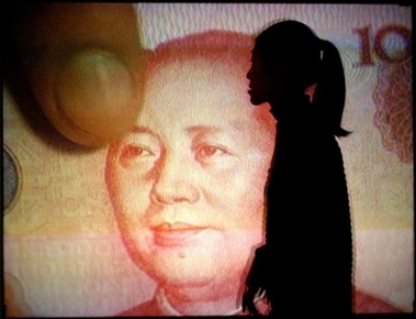 A Chinese woman is silhouetted near a video screen displaying an enlarged image of Chinese currency during an exhibition in Beijing, China, in this October 7, 2003, file photo. 
