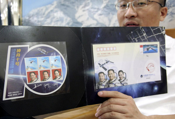 A man shows a stamp folder containing an envelope and three stamps with the portraits of three astronauts to be carried by Shenzhou-X, China’s fifth manned spacecraft to be launched Tuesday, June 10, 2013. Stamps commemorating Shenzhou X manned spacecraft issued