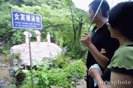 A couple reads a blue notice sign that says Nude Swimming Allowed for 