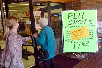 A cancelled flu shots sign at Thrifty White Drug in Mandan, N.D., Tuesday, Oct. 19, 2004, lets two unidentified customers know that the vaccine was recalled by the manufacturer. With a shortage of vaccine shutting down flu shot clinics around North Dakota, some are considering a trip to Canada. [AP]