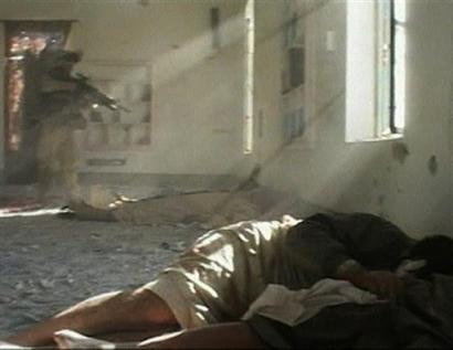 In this image taken from pool video provided to the Associated Press by NBC News, a U.S. marine is seen, left, raising his rifle in the direction of Iraqi prisoners lying on the floor of a mosque in Fallujah, Iraq Saturday Nov. 13, 2004. The pool video was recorded Saturday as the Marines returned to an unidentified Fallujah mosque. The video, in a version aired by CNN showed the Marine raising his rifle toward the prisoners but neither NBC nor CNN showed the shooting itself. The video was blacked out but the report of the rifle could be heard. The bodies in the foreground are other Iraqi prisoners. [AP]