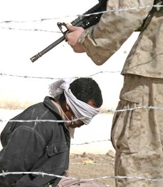A blindfolded detainee is guarded by a U.S. Marine following his arrest in the war-torn western city of Falluja, November 23, 2004. Iraq's U.N. representative, Samir Shakir Sumaidaie, said that attacks on insurgents in Falluja made it easier to hold the elections because it had destroyed the base and infrastructure of groups seeking to rule the country.