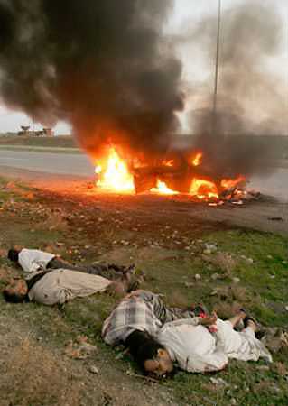 The bodies of four men lie close to a burning pickup truck at the side of a highway near the northern Iraqi city of Mosul, December 14, 2004. The bodies of six young men, all shot in the head as if executed, were discovered in Mosul on Tuesday, bringing the total of such corpses found to 14 in two days. The vehicle was attacked and burned one hour after the men had been shot, witnesses said. [Reuters] 