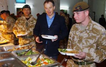 British Prime Minister Tony Blair (C) has dinner with British soldiers at a military camp in the southern Iraq city of Basra December 21, 2004. Blair acknowledged the grave dangers in Iraq when he made a surprise visit to Baghdad on Tuesday, but the British Prime Minister vowed that the war against insurgents would be won and elections held on time. [Reuters]