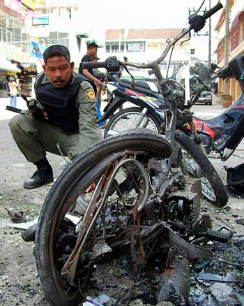A Thai soldier inspects a destroyed motorcycle in front of Siam Commercial Bank in Sungai Kolok district, Narathirat province, about 1149 km (652 miles) south of Bangkok, December 24, 2004. A bomb hidden in a motorcycle killed one person and wounded six outside a bank in Thailand's largely Muslim deep south on Friday, police and hospital officials said. [Reuters]