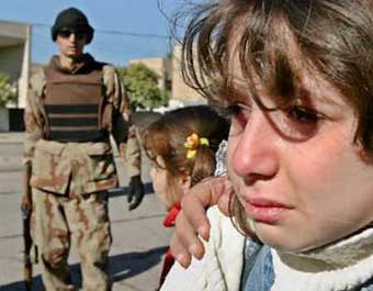  seven year-old Iraqi girl cries near an armed guardsman after a car bomb exploded near her school in northern Baghdad, December 28, 2004. A car bomb targeting a senior officer in the U.S.-backed Iraqi National Guard killed one person and injured eight, witnesses and a police source said.