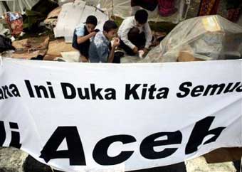 Refugees have breakfast in the tent as a sign says 'All the sympathy for Aceh' at a refugee camp Saturday, Jan 1, 2005 at the airport in Banda Aceh, the capital of Aceh province, as survivors survey the devastation of the earthquake-triggered Tsunami that killed at least 80,000 people in the province alone in northwest Indonesia and raised the death toll across Asia to more than 100,000. (AP