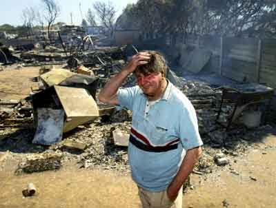 Local resident Bob Arthur stands in front of what remains of his belongings after a bushfire engulfed the caravan park he lived in near the town of Port Lincoln on the Eyre Peninsula in South Australia January 11, 2005. At least five people are now confirmed dead as fires continue to rage across lower Eyre Peninsula, located around 600 kilometres northwest of Adelaide, heading towards coastal townships. [Reuters]