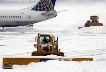 Crews work to clear snow from the tarmac as a plane sits idle at a gate Sunday, Jan. 23, 2005, at Logan International Airport in Boston. Whiteout conditions grounded airplanes and sent fleets of plow and salt trucks trundling through snow-clogged roadways before the storm began to ebb at midday. (AP 