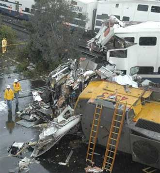 Workers walk around a train derailment, Wednesday, Jan. 26, 2005, that occured after a suicidal man parked his SUV on the railroad tracks and set off a crash of two commuter trains Wednesday that hurled passengers down the aisles and turned rail cars into smoking, twisted heaps of steel, authorities said. At least 10 people were killed and more than 180 injured (AP 