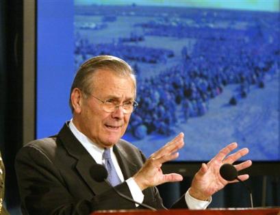 With a photo of lines of Iraqi voters in the background, Defense Secretary Donald H. Rumsfeld gestures during a Pentagon news conference, Thursday, Feb. 2005 to discuss the situation in Iraq. [AP]