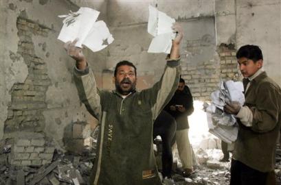 A guard holds up religious papers amongst rubble at the Tawhid Mosque, which was the target of an attack in Baghdad, Iraq Friday, Feb. 4, 2005. Gunmen entered the Shiite mosque, ordering a few guards to leave the building and then placed explosives inside, resulting in the hole being blown in the Mosque's wall. [AP]