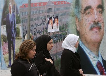 Lebanese women pass next to a mural of Lebanon's slain former prime minister Rafik Hariri covered with poems and condolences from wellwishers near his grave in Beirut, Lebanon, Sunday, Feb. 20, 2005. After the murder Monday of the Sunni Muslim former prime minister, and especially at his funeral two days later, Christians, Muslims and Druse came together in a vivid manifestation of unity rare in Lebanon's history. [AP]