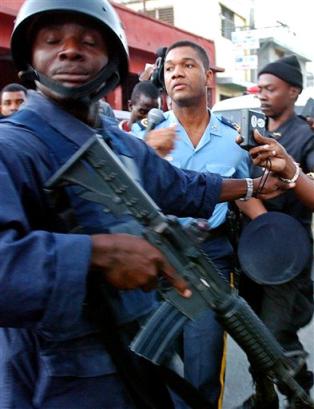 Haitian Civil Prison Director Claude Theodate, center, is escorted by Haitian police following an armed breakout at the prison in the Rue Centre neighborhood of Port-au-Prince, Haiti, in this picture taken Saturday, Feb. 19, 2005. Theodate was fired from his position as director of the Haitian Civil Prison, as the Haitian government investigates the escape of 481 prisoners in Saturday's bloody prison break. [AP]