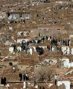 Iranian villagers stand on a hillside in the ruins of the village of Dahouyeh, 9 miles north of Zarand, February 22, 2005 after a tremor with a magnitude of 6.4 struck the region. A powerful earthquake struck southeast Iran, killing 400 people, injuring hundreds and turning remote mountain villages into rubble, officials said. Photo by Raheb Homavandi/Reuters 