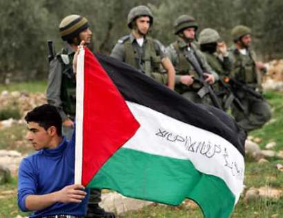 A Palestinian youth holds a Palestine flag in front of Israeli border police during a protest against Israel's controversial security barrier near the West Bank village of Bilin March 8, 2005. Palestinian President Mahmoud Abbas accused Israel of undermining peace efforts by dragging its feet over promises to free prisoners and pull back from West Bank cities. [Reuters] 