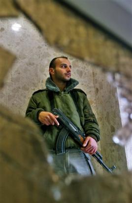 A Palestinian security guard is seen through shattered window, broken when more than 20 Palestinian gunmen burst into a large gathering of the ruling Fatah party in a Ramallah hotel Thursday March 10, 2005. [AP]