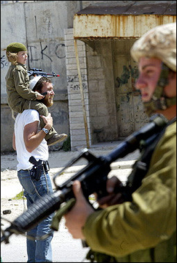 An Israeli soldier stands guard as a settler and his child disguised as a soldier celebrate Purim in the divided West Bank city of Hebron. [AFP]