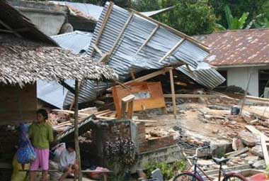 Residents sit near a house damaged by earthquake in Nias island, Indonesia, Tuesday, March 29, 2005. The small Indonesian island bore the brunt of an 8.7-magnitude undersea earthquake that struck late Monday, burying an unknown number of people beneath their homes as they collapsed three months after a massive temblor in the same offshore region west of Sumatra sent tsunami waves crashing into a dozen countries on the Pacific Ocean's rim, killing more than 174,000.. (AP 