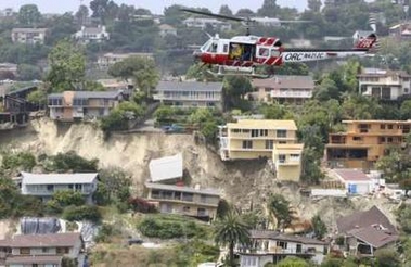 An Orange County fire department helicopter flies past houses that were damaged during an early morning landslide in Laguna Beach, California, June 1, 2005. Police said 15 to 18 homes were destroyed or seriously damaged and about 20 others were destabilized by the slide that happened just before 7 a.m. as residents were getting up and preparing to go to work or school. The occupants of the helicopter were taking a closer look at the damage. REUTERS