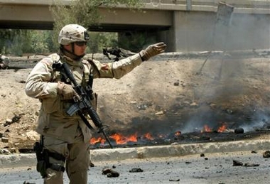 A U.S. soldier stands guard on the street in front of burning debris left after a suicide car bomb attack in Baghdad, Iraq Saturday, June 18, 2005. The suicide car bomber slammed into an Iraqi army convoy, killing two soldiers and wounding six near a hazardous highway that leads from downtown Baghdad to the airport. (Ap 