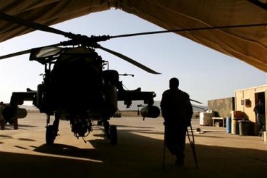 A soldier who hurt his leg while jumping from a helicopter on a mission walks nearby an AH-64 Apache helicopter in the air base of Kandahar, southern Afghanistan, Friday, June 24, 2005. Fighting intensified in the south of Afghanistan this week, where tens of insurgents are reported dead. (AP
