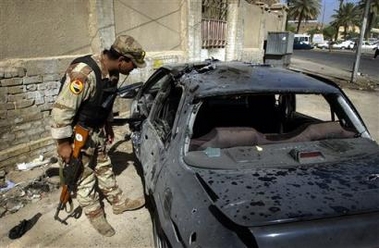 An Iraqi soldier looks at the remains of a car which was damaged in a road side bomb attack in Baghdad, Iraq Monday, June 27, 2005. The attack, aimed at a passing Iraqi police patrol, killed two civilians and injured another, according to Iraqi police. (AP