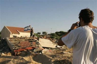 An Israeli security officer in civilian clothes takes a snapshot of a colleague holding an Israeli flag on top of a demolished house in the Jewish settlement of Peat Sadeh, southern Gaza Strip, Sunday, Aug. 21, 2005. Israeli bulldozers leveled homes in three Gaza settlements Sunday, reducing once-thriving villages within hours to refuse dumps and sealing the fate of Jewish settlement in the coastal strip. The military plans to raze all Gaza settlement houses within two weeks. [AP]