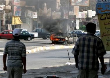 Pedestrians approach a burning police vehicle in the western Baghdad neighborhood of Khadra after a firefight between insurgents and Iraqi police, Wednesday, Aug. 24, 2005. Insurgents attacked Iraqi police patrols in western Baghdad on Wednesday with at least three car bombs and small arms fire, killing at least five people and wounding 19, police said. (AP 