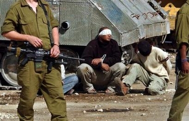Detained Palestinians sit on the ground next to an armored vehicle as Israeli troops stand guard during a military raid in the West Bank town of Tulkarem, Monday Oct. 24, 2005.