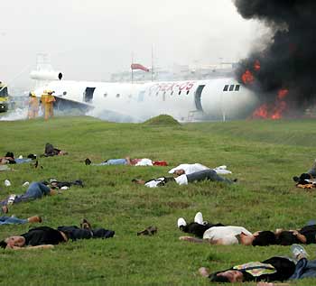 Filipinos lie on a grassy area, playing the role of wounded passengers, while firefighters douse a fire using chemicals on a mock plane during a crash rescue exercise at the tarmac of the Manila International airport November 9, 2005.