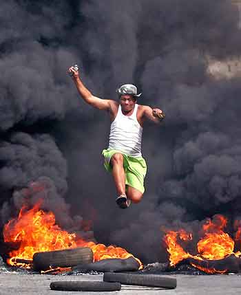 A Philippine resident jumps to avoid burning tyres which were set on fire by protesters to block anti-riot policemen and members of a demolition team tearing down their homes at St. Joseph compound in Sun Valley, Paranaque city, south of Manila, November 14, 2005. Unrest erupted in the area on Monday after more than 200 families, who said they had government permission to occupy more than 1.2 hectares of land, tried to stop demolition teams tasked to clear the area by the land's private owner.