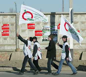Young men carry flags of the liberal Yabloko party as they walk past a wall with election posters in Chechnya's capital of Grozny November 24, 2005. An election in Chechnya this weekend is the final stage in a Kremlin plan to make the turbulent region a normal part of Russia.