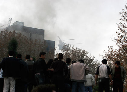 eople watch a rescue helicopter taking off near an apartment block after an Iranian military plane crashed into it Tehran December 6, 2005. 